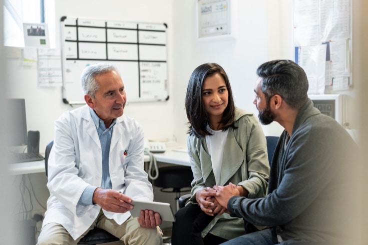 Doctor Discussing RPM Readings With Couple Over Digital Tablet