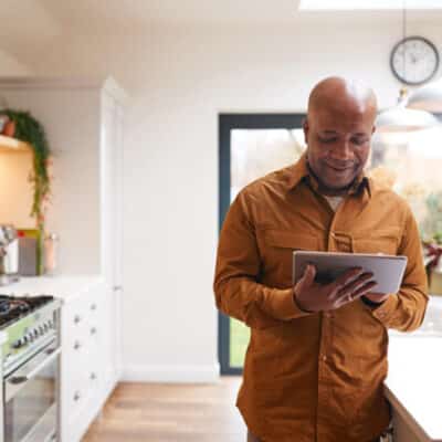 Man In Kitchen Checking Readings On Tablet