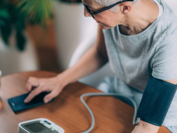 Woman taking blood pressure and checking results on phone