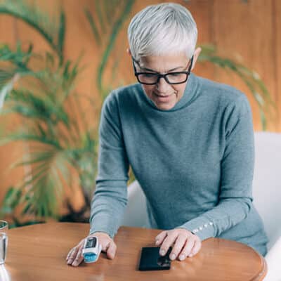 Woman Using Pulse Oximeter And Checking Readings On Phone